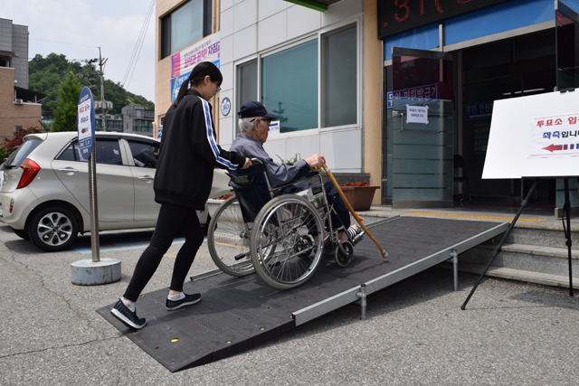양재석(88) 어르신이 명륜2동행정복지센터에 마련된 투표소를 방문하기 위해 자원봉사자의 도움을 받으며 휠체어를 타고 경사로를 오르고 있다.