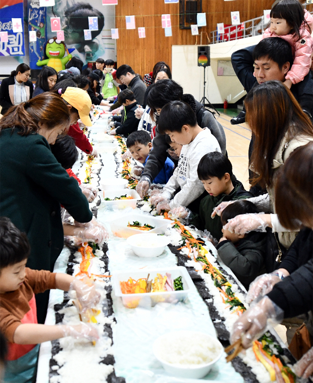 ▲ 속초시건강가정·다문화가족지원센터(센터장 김상래)가 18일 속초시생활체육관에서 진행한 ‘2018년 아름다운 동행,우리는 한가족’ 행사 참가자들이 대형 김밥을 만들고 있다.