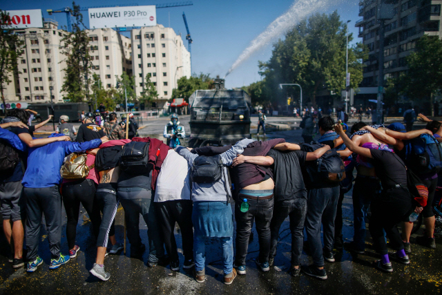 ▲ Demonstrators make a line as riot police repel with a water cannon during protests in Santiago, on October 20, 2019. - Fresh clashes broke out in Chile‘s capital Santiago on Sunday after two people died when a supermarket was torched overnight as violent protests sparked by anger over economic conditions and social inequality raged into a third day. (Photo by Pablo VERA / AFP)    <All rights reserved by Yonhap News Agency>