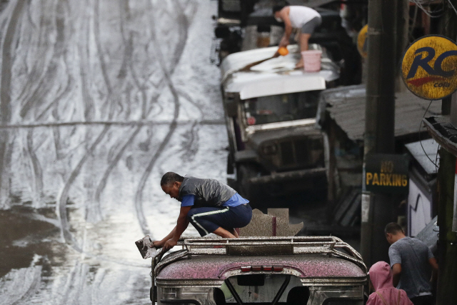 ▲ Residents clean ash from their vehicles from Taal Volcano‘s eruption Monday Jan. 13, 2020, in Tagaytay, Cavite province, south of Manila, Philippines. small volcano near the Philippine capital that draws tourists for its picturesque setting in a lake erupted with a massive plume of ash and steam Sunday, prompting the evacuation of tens of thousands of people and forcing Manila’s international airport to shut down. (AP Photo/Aaron Favila)    <All rights reserved by Yonhap News Agency>